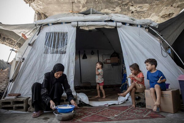 Mulher prepara alimento diante de uma barraca com crianças no campo de Al Saraya, em Gaza