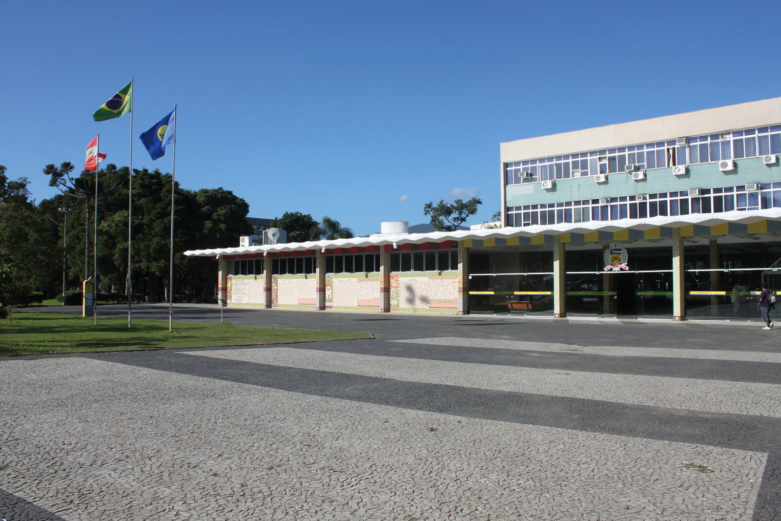 Prédio da Reitoria da UFSC, com bandeiras e a Praça da Cidadania em primeiro plano, em Florianópolis.